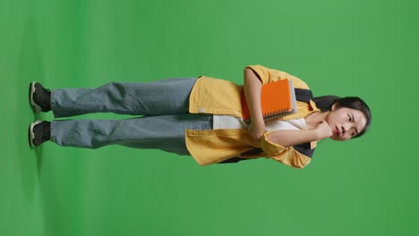 full body of asian woman student with a backpack and some books thinking and looking around then raising her index finger while standing in the green screen background studio