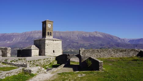 historic clock tower of gjirokastra's castle and ruined stone walls with mountain background