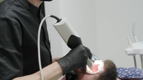 doctor scans the patient's teeth in the clinic. the dentist holds in his hand a manual 3d scanner for the jaw and mouth. dental health. creates a 3d model of teeth and gums on a medical monitor.