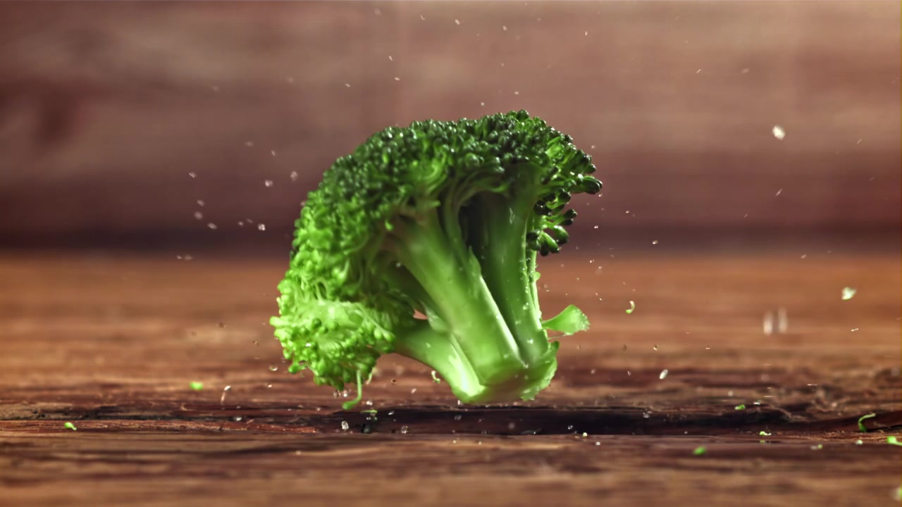 Movimento rallentato di una cimetta di broccolo fresco che cade su una superficie di legno