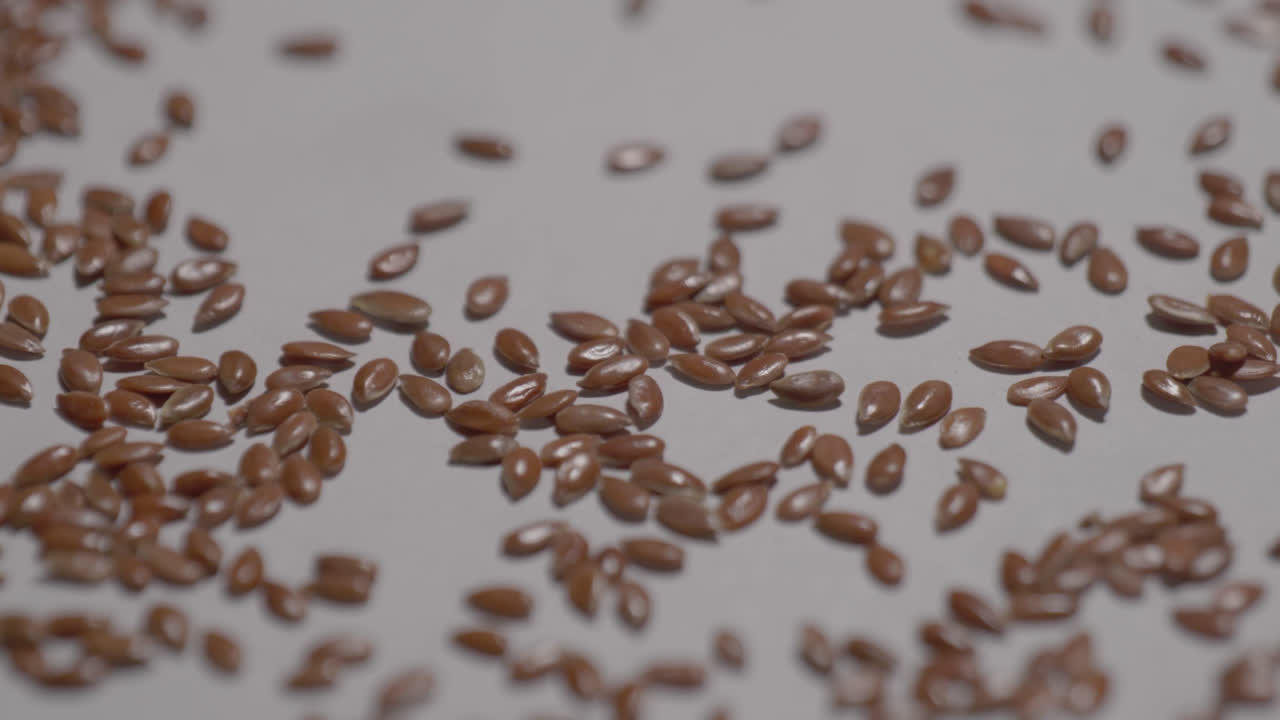 flax seeds falling on white surface, 4k, stable shot