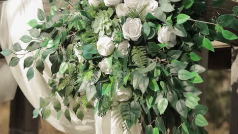 beautiful close up of a wedding arch with a white and green bouquet hanging from top of it and white drapes hung over the top
