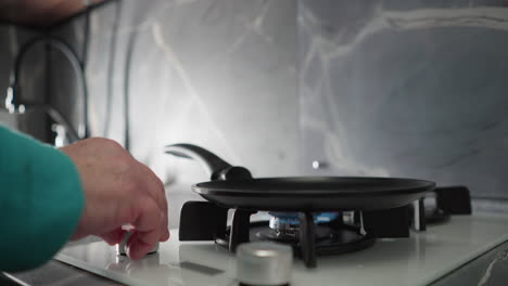 close-up shot of elderly woman in green adjusting gas stove burner in modern kitchen. focus on her hand turning burner knob with sleek black and white kitchen design in background