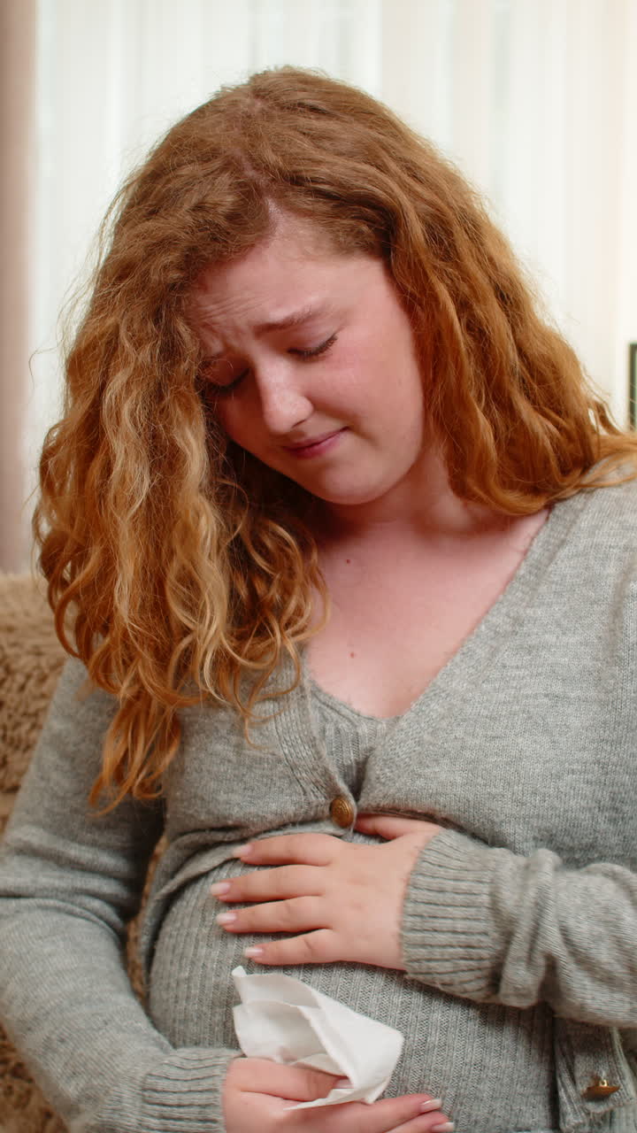 Pregnant young woman wiping tears at home holding belly emotional and sensitive moment of pregnancy