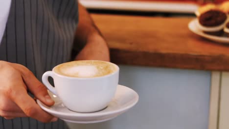 primer plano del camarero sosteniendo una taza de café en el mostrador