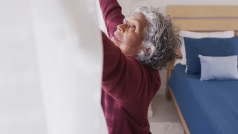 Happy-senior-african-american-woman-widening-curtains-in-bedroom