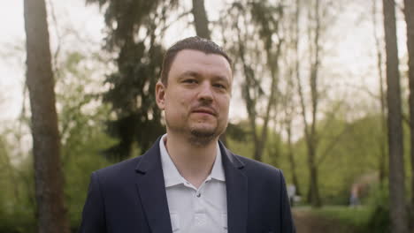 retrato de um homem elegante olhando para a câmera e sorrindo em pé no parque