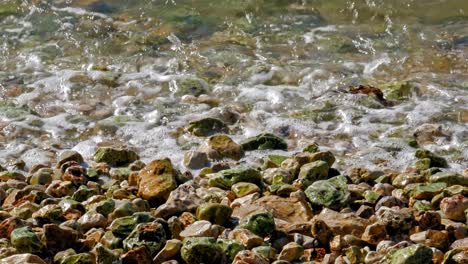 waves crash onto a rock and pebble beach - jerusalem beach in greece - high angle shot