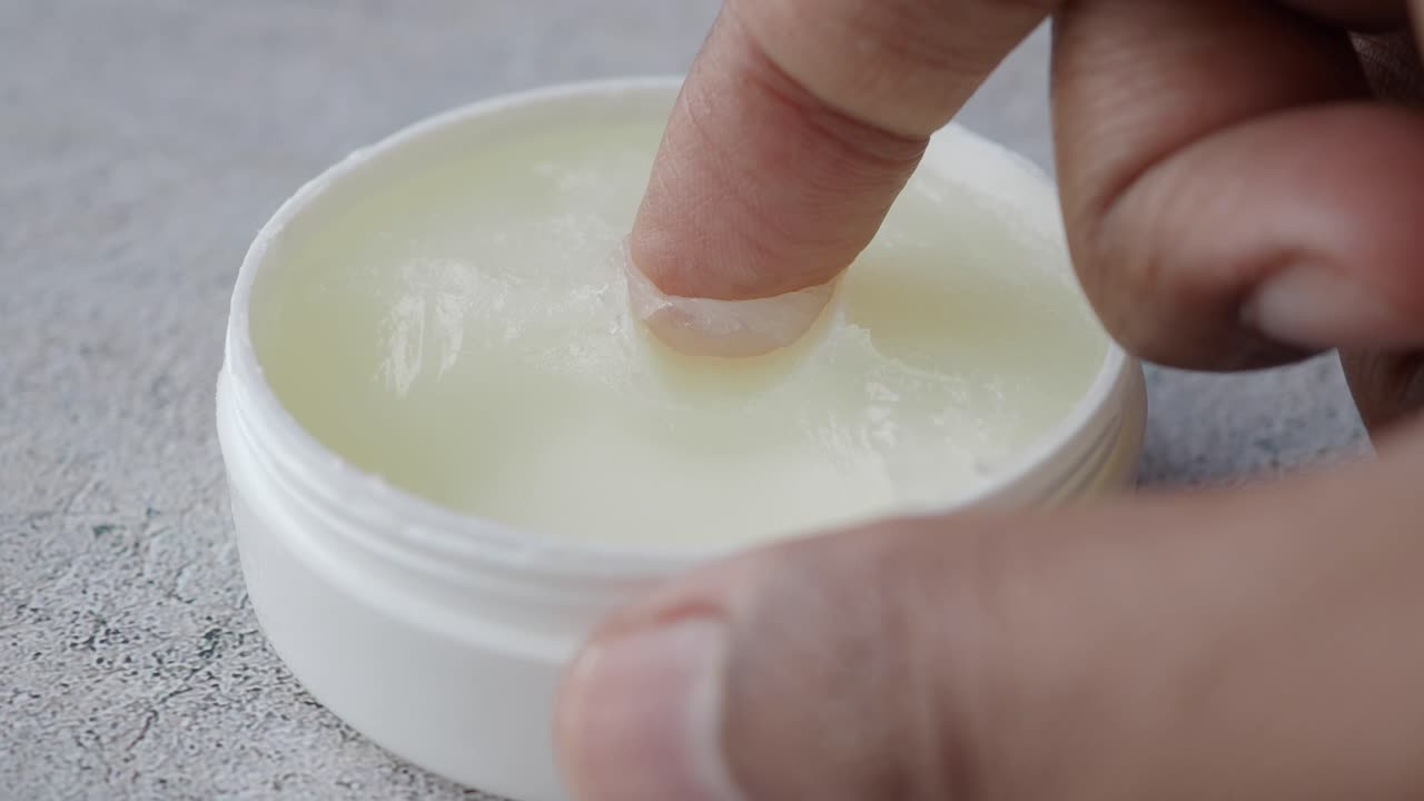 primer plano de una mano aplicando crema de un frasco