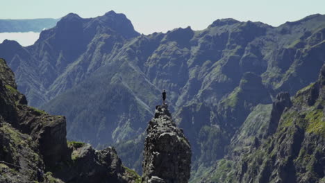 zooming in to man standing on small rock outcrop overlooking volcanic mountains