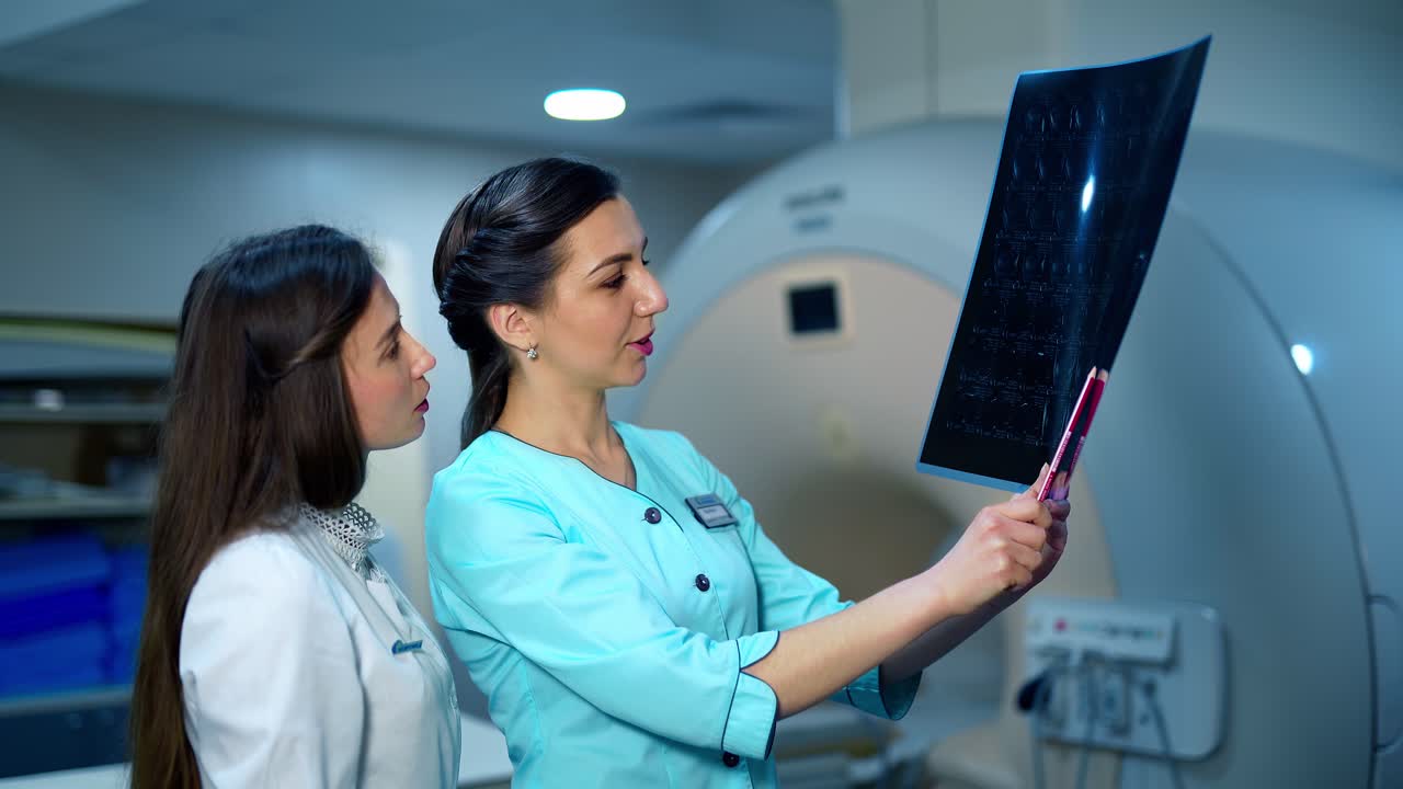 Female specialists analyze the x-ray photo. Medical workers examining radiography picture and talking about patient's disease in advanced clinic.