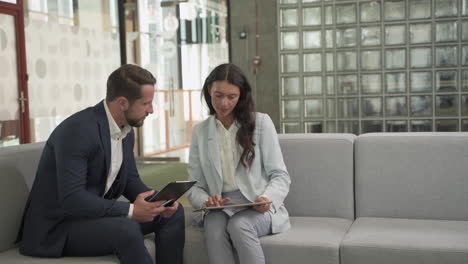 A-Young-Businessman-With-Beard-And-Suit-Has-A-Business-Meeting-With-A-Pretty-Young-Businesswoman-On-The-Sofas-In-The-Common-Area-Of-The-Office-Building-2