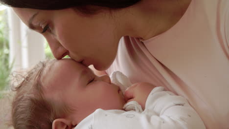 mother kissing sleeping baby boy at home