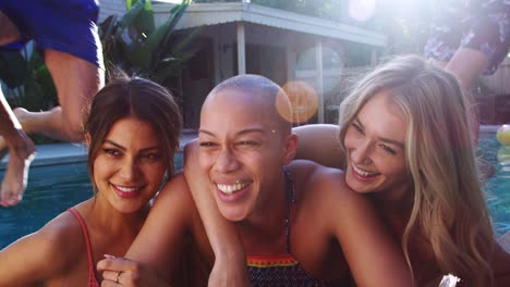 Female-Friends-Outdoors-Relaxing-At-Summer-Pool-Party-As-Men-Dive-In-And-Splash-Behind-Them