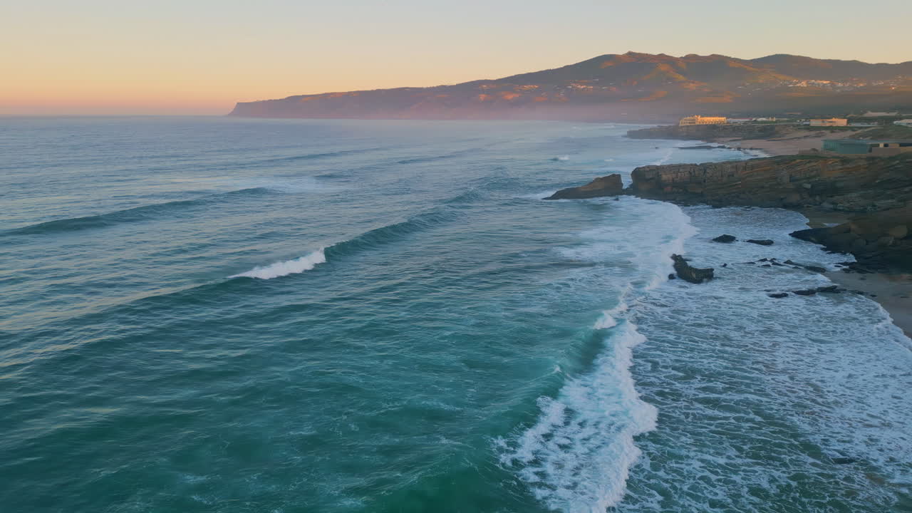 Aerial view amazing ocean rolling on coastal rocks at sunrise. Foamy sea waves