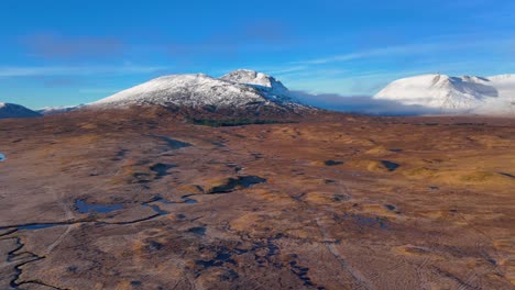 aerial panning shot of streams running through a moor with snow covered mountains