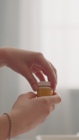 Lady artist turns cap to open bottle with sparkling yellow paint near window slow motion. Woman works in art studio. Supplies for artistic work