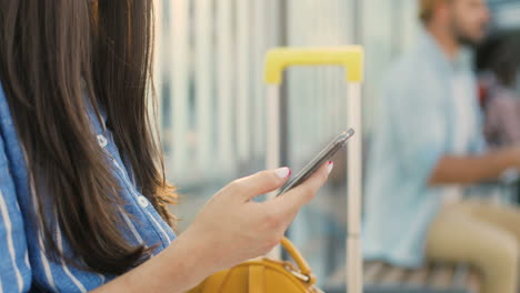 Close-up-view-of-Caucasian-female-traveller-hand-holding-smartphone-and-tapping-on-screen-outdoors