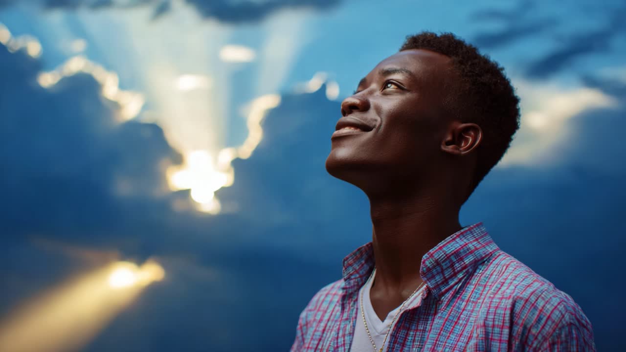 A young man stands in awe under a dramatic sky, illuminated by rays of sunlight breaking through the clouds, expressing a sense of wonder and serenity in a moment of contemplation and inspiration