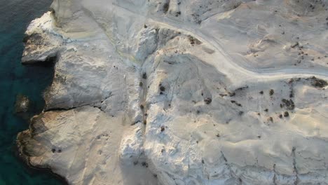 drone view in greece flying over a moon shaped white rock and clear blue water top view in milos island at sunrise next to the dark blue sea