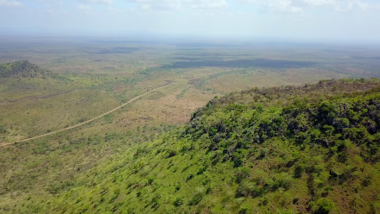 Breathtaking aerial perspective showcasing the vast, mountainous landscape of Karamoja, Uganda, featuring lush vegetation, a winding road, and a serene valley under a soft daytime sky