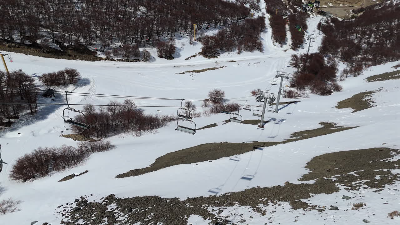 Downward drone shot of ski chair lifts at La Hoya resort in Esquel, Argentina. High contrast between soil, background trees and snow. 4K-60fps.
