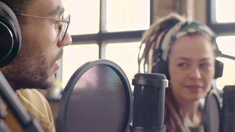 close up view of young wearing headphones sitting at a table with microphones while recording a podcast with woman