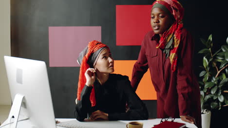 female muslim coworkers talking by desk