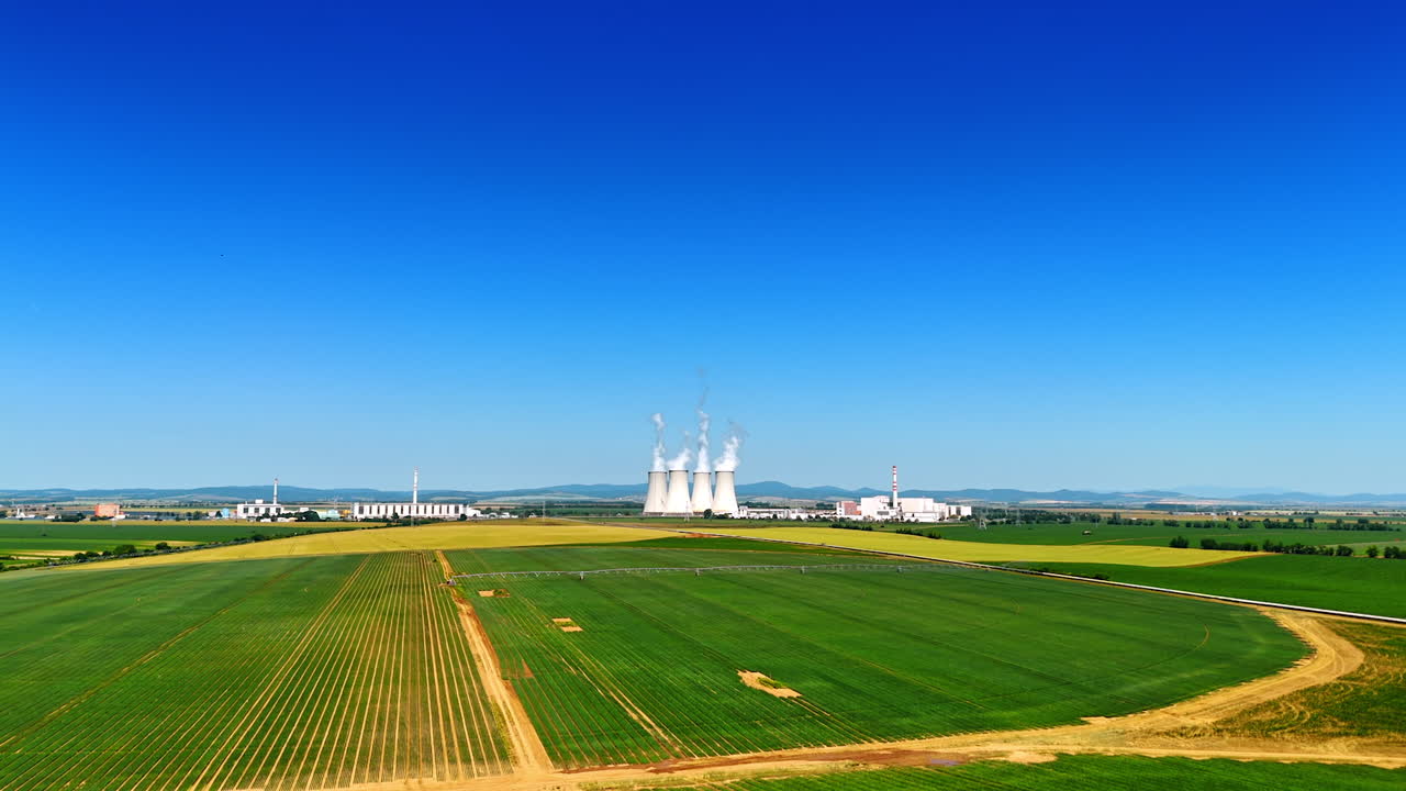 Power plant amid a green landscape. A power plant stands prominently against a clear blue sky, surrounded by vibrant green fields and distant hills