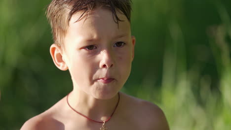 portrait of a cute hungry boy outdoors. little boy with wet hair is eating something on blurred background in summer.