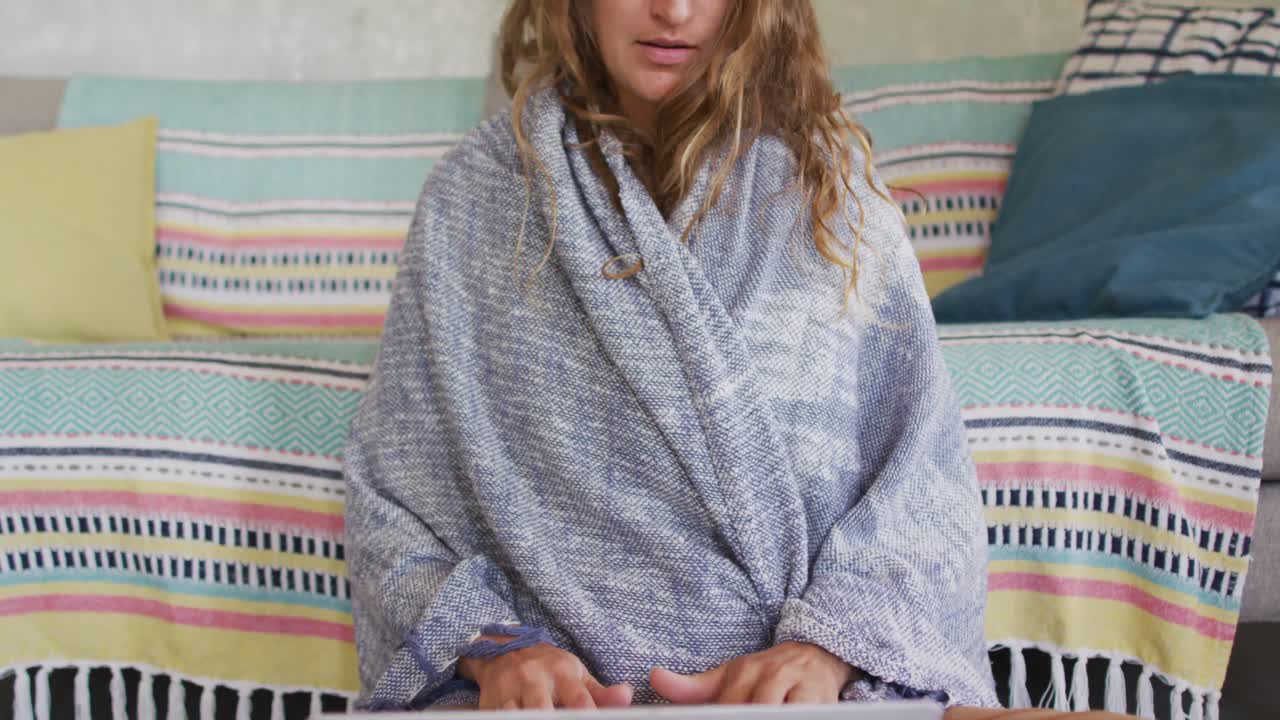 코티지 거실에서 노트북을 사용하여 담요를 입고 바닥에 앉아 있는 사려 깊은 백인 여성