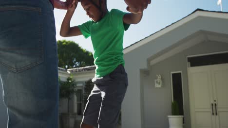 african american dad teaching his son to skateboard in the front yard