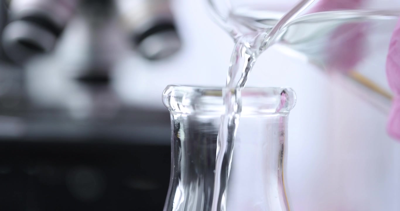 Liquido trasparente scorre in un becher di vetro con riflessi