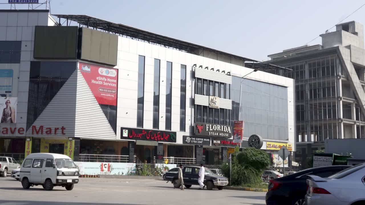 A remarkable commercial building looms tall on the main road, surrounded by parked cars in the front.