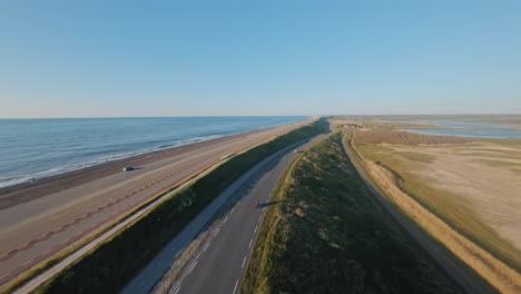 aerial tracking shot of a motorcyclist on an asphalt coastal road on a dike along a blue sea on a beautiful sunny day