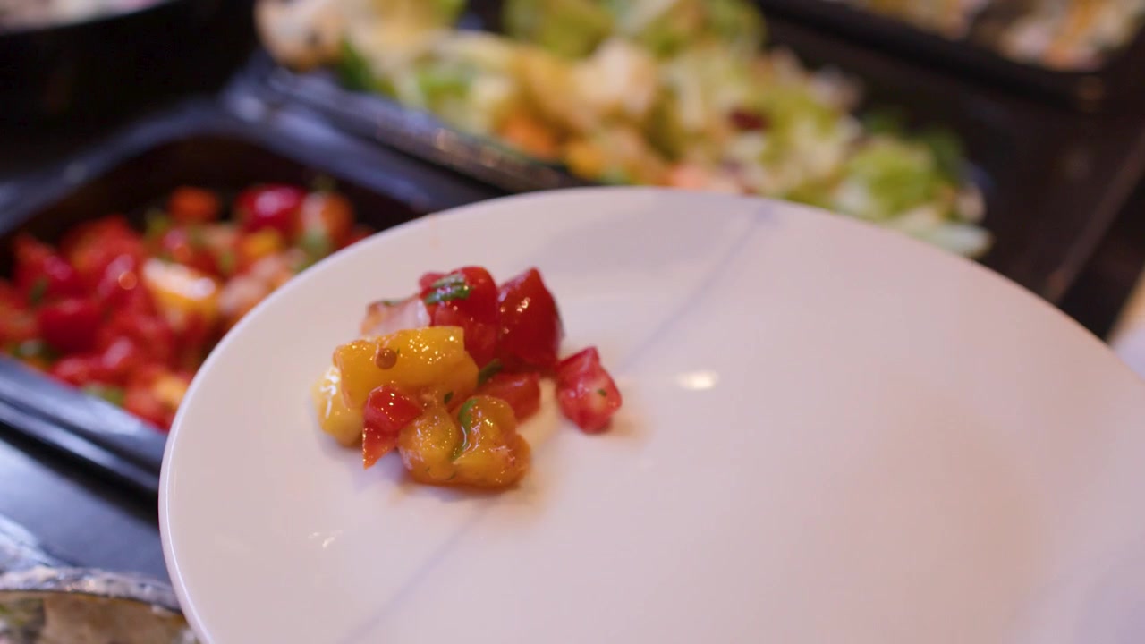 Primo piano di mani che usano pinze nere per posizionare salsa fresca su un piatto bianco