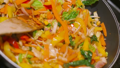 top rotating view of colorful oriental stir fry vegetables in hot wok pan including carrots, beansprouts, peppers, onions