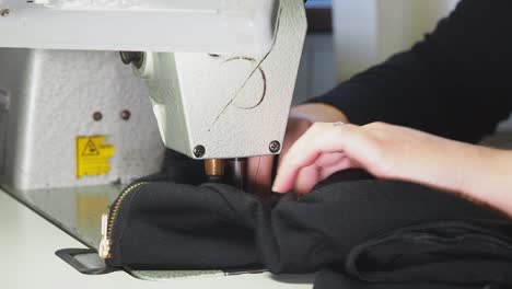 a woman using the sewing machine and sewing some black fabric