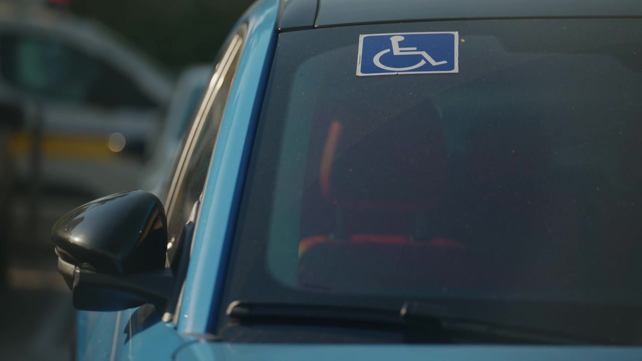 Permesso di parcheggio per disabili esposto sul parabrezza di un'auto blu parcheggiata in una strada cittadina.