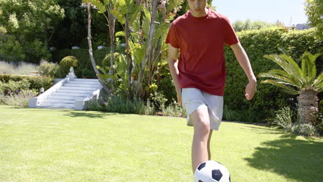 Hombre-Birracial-Enfocado-Practicando-Habilidades-Con-Fútbol-En-Un-Jardín-Soleado,-Espacio-Para-Copiar,-Cámara-Lenta