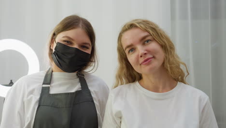client and technician stand side by side looking at camera in modern salon setting, with tools neatly arranged on table, ring light glowing behind, and both showing calm, satisfied expressions