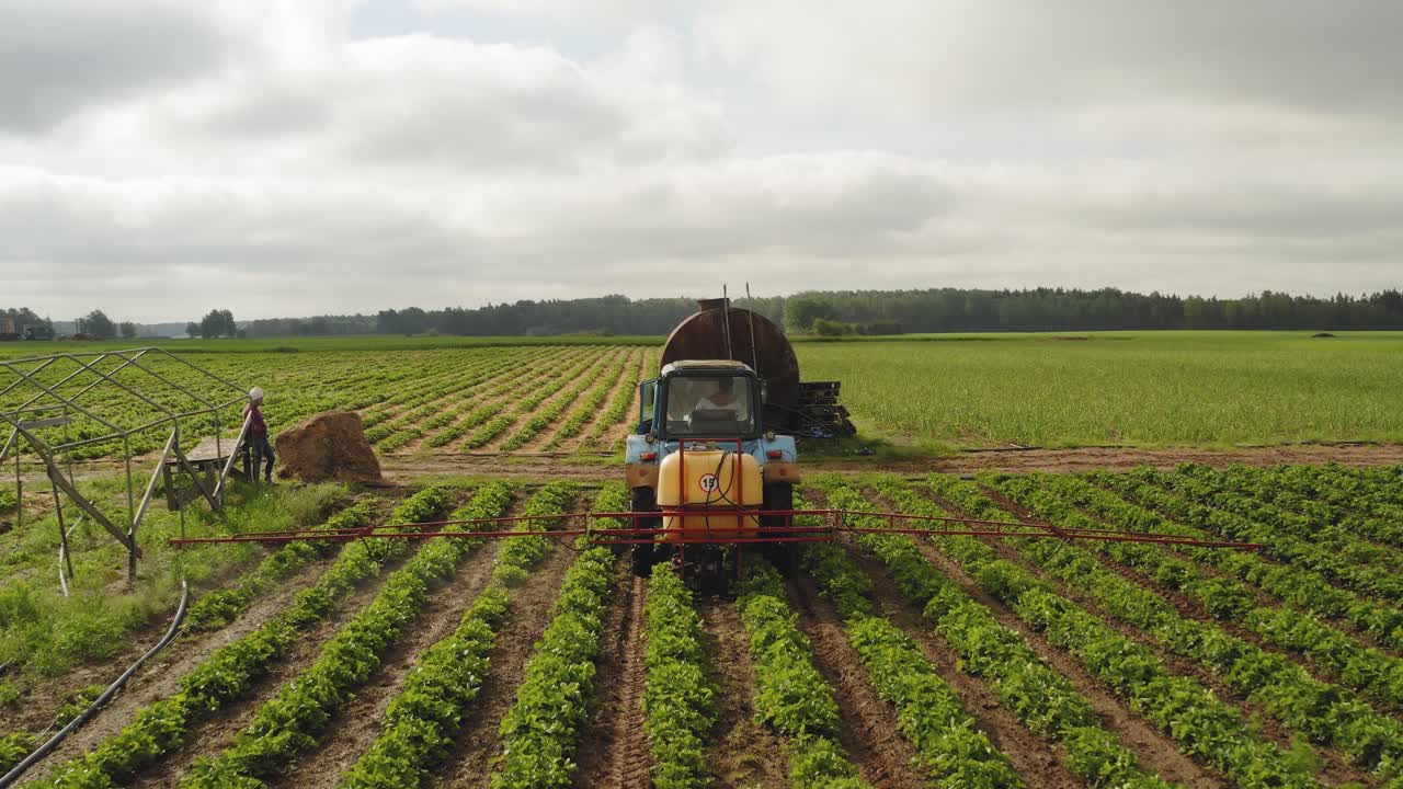 Toma aérea siguiendo desde atrás a un tractor fumigando un campo de fresas contra enfermedades