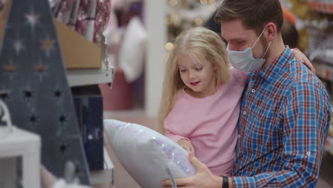 un padre con una máscara médica en la cara con su hija elige joyas y juguetes en la víspera de navidad para decorar la casa y el árbol de navidad