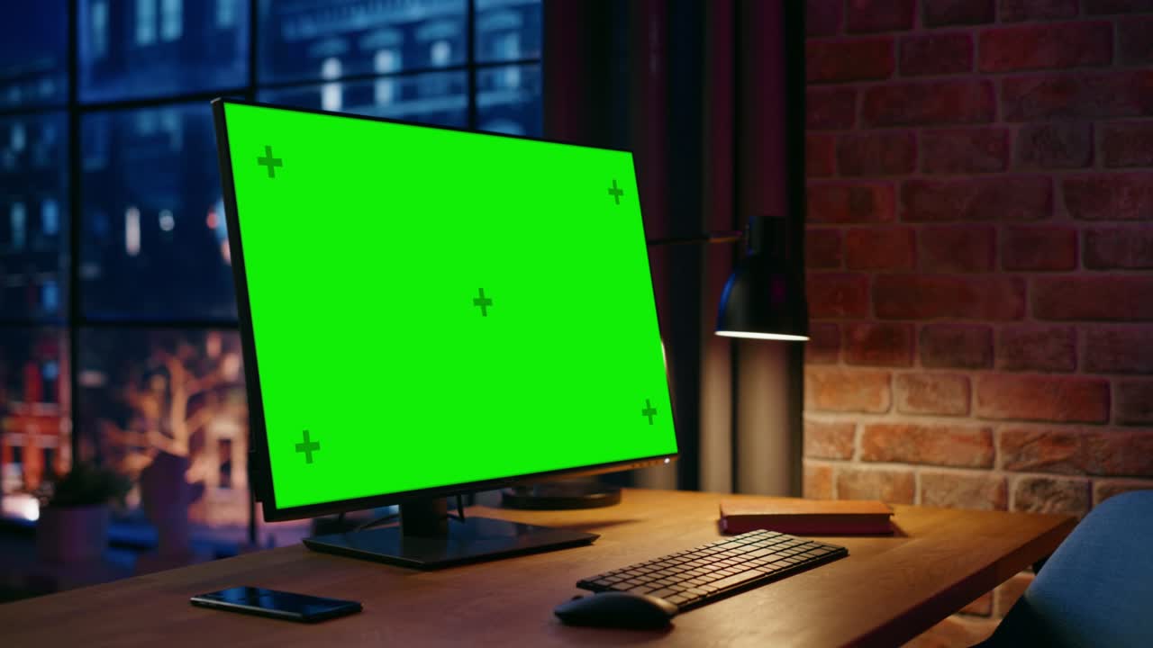 monitor computer desktop in piedi su un tavolo con uno schermo verde chromakey mock up display. accogliente appartamento vuoto loft con grande finestra con una lampada, notebook e smartphone sul tavolo. tiro ad arco.