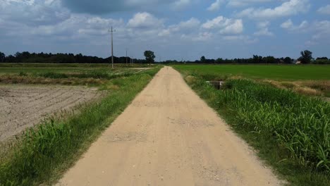 Drohnen-Pov-Beim-Gehen-Auf-Einem-Einsamen-Pfad,-Einer-Verengten-Straße-Auf-Dem-Land-Mit-Landwirtschaftlichen-Flächen