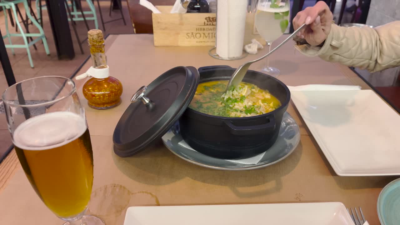 Pot of soupe served on a table by a waiter and stirred by a woman. Static