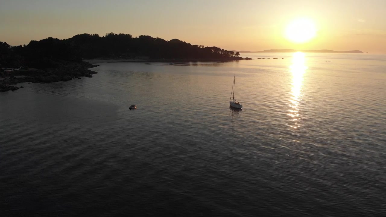 Ripresa aerea di uno yacht locale ancorato nelle calme acque basse della spiaggia di Bueu in Galizia, Spagna. Onde dolci e un sole caldo e rilassante rendono la visita invitante.
