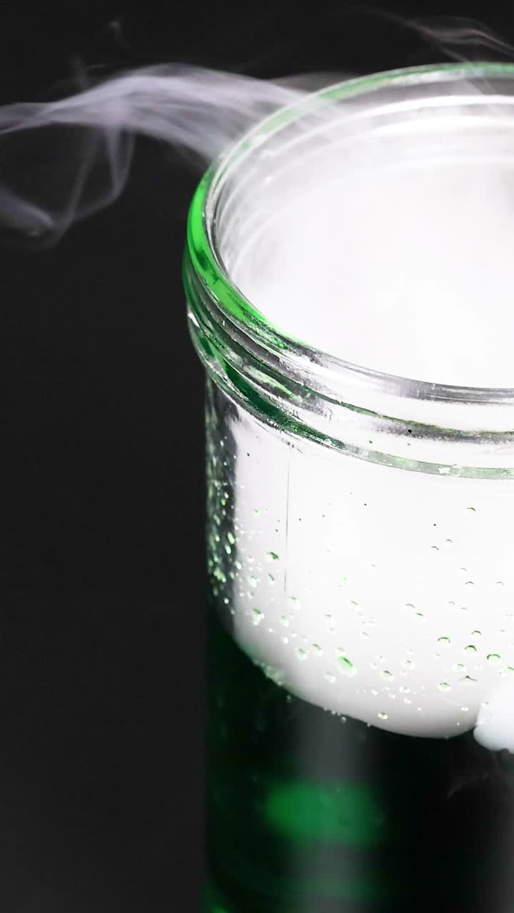 un vaso con hielo seco crea una reacción nebulosa en líquido verde, mostrando un experimento científico