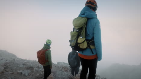 Hikers-with-helmets-and-backpacks-try-to-look-into-the-valley-throug-the-mist-and-clouds-in-early-morning