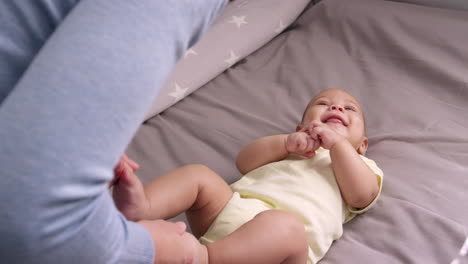 mother playing with baby son lying on bed in nursery